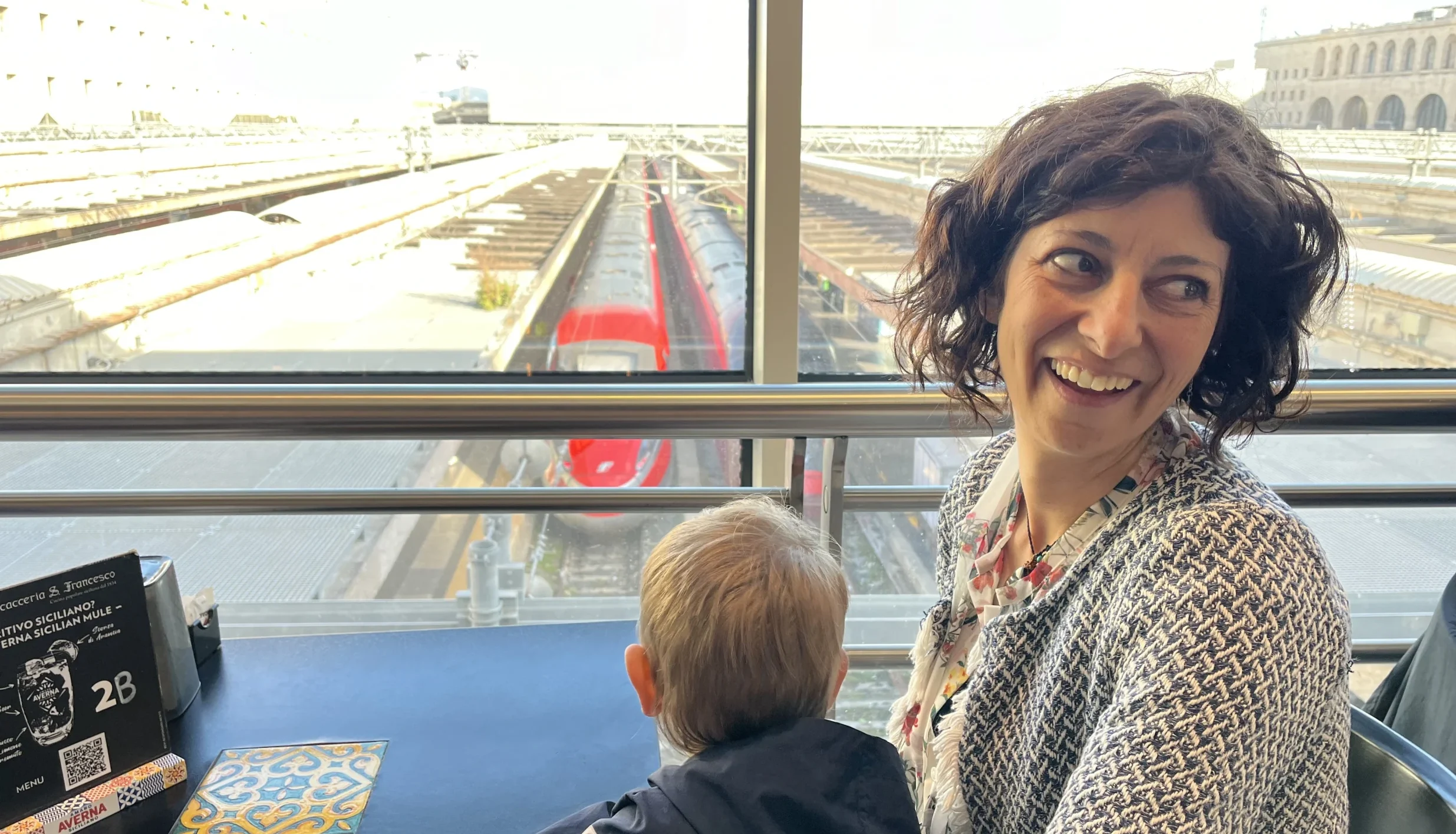Maurizia ride con in braccio Ethan alla foud court della stazione di Roma termini con sotto i binari con Freccia Rossa e Italo.